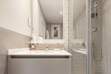 Designer bathroom with marble sink under a mirror built into the wall and shower with tempered glass screens