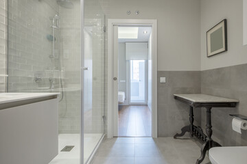 Fototapeta na wymiar Designer bathroom with marble sink under wall-mounted mirror and shower with tempered glass partitions and access door to an en-suite bedroom