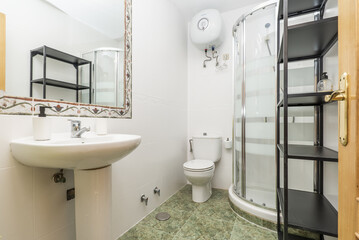 Bathroom with white porcelain one-piece pedestal sink and valance-framed wall mirror, corner shower stall and black metal shelving