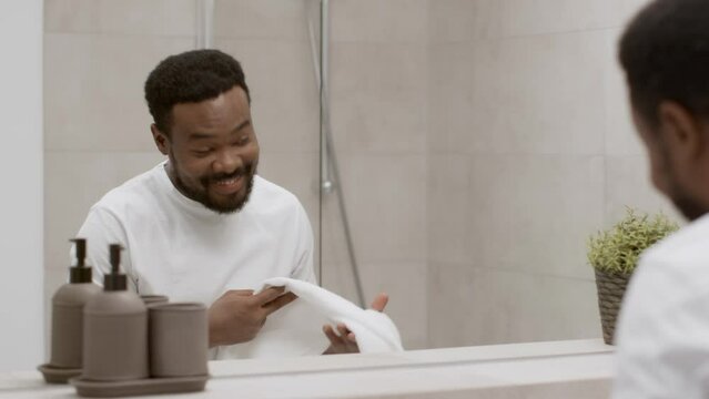Morning motivation. Young handsome african american guy washing face in bathroom and smiling to reflection, empty space