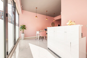 White wooden reception desk in a local beauty salon with pink walls, black metal and glass showcase and white marble floors