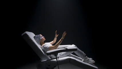 Woman having VR experience zoom on. Girl using sensor gloves sitting armchair