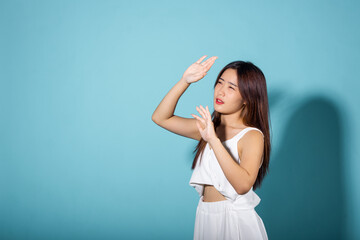 Female raising arm and hand in protection and block sunshine in studio shot isolated on blue background, Asian young woman smile hand up cover face protect sun light and UV, sunscreen cream advertise