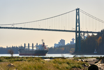 Cargo Freighter Under Lions Gate Bridge. A large cargo container ship cruises into Vancouver harbor under the Lions Gate Bridge at sunrise. British Columbia, Canada.

