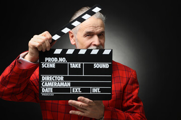 Senior actor with clapperboard on black background. Film industry - obrazy, fototapety, plakaty