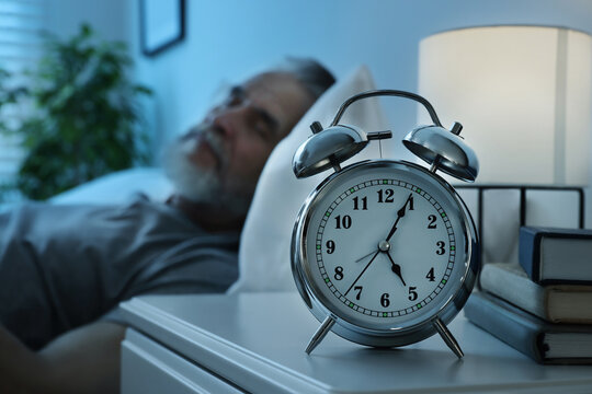 Senior man sleeping in bed at home, focus on alarm clock. Space for text