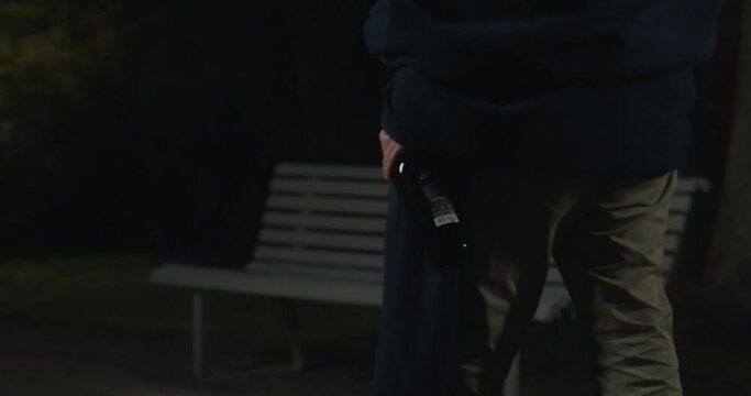 alcoholic walks through the park at night with a bottle in his hand. Slow-motion footage.