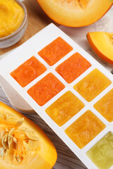Fototapeta na wymiar Different purees in ice cube tray ready for freezing and fresh pumpkin on table