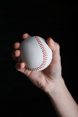 Baseball player holding ball on black background, closeup. Sports game