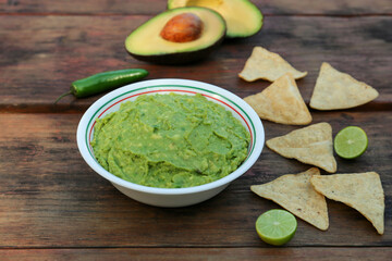 Delicious guacamole made of avocados with nachos on wooden table