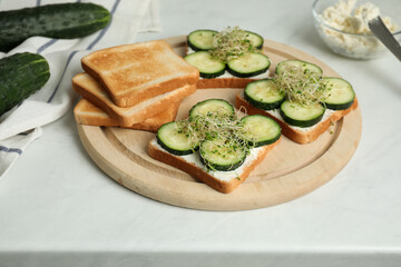 Tasty toasts with cucumber, cream cheese and microgreens on white table