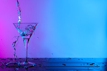 Pouring fresh martini into glass on table in neon lights, space for text