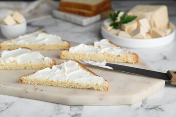 Delicious toasts with tofu cream cheese and knife on white marble table, closeup