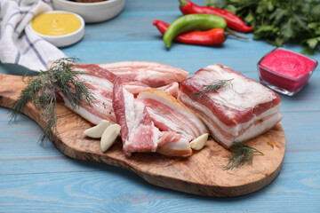 Pieces of pork fatback with garlic and dill on light blue wooden table