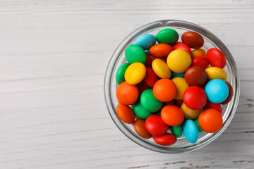 Bowl with tasty colorful candies on white wooden table, top view. Space for text