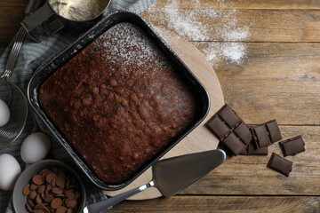 Homemade chocolate sponge cake and ingredients on wooden table, flat lay