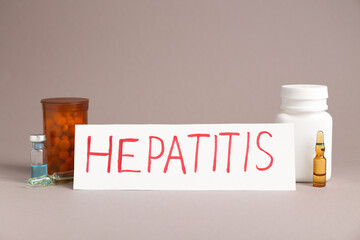 Word Hepatitis, vials and bottles of pills on beige background