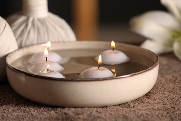 Burning candles in bowl with water on massage table, closeup