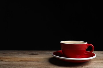 Red ceramic cup with hot aromatic coffee on wooden table against black background, space for text
