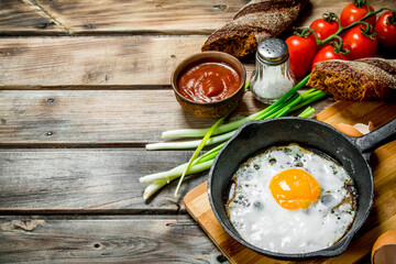 Obraz na płótnie Canvas Fried egg in a pan with bread, tomatoes and green onions.