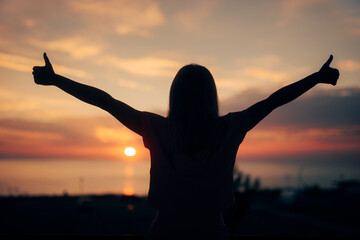 Backlit silhouette of a Woman Holding Thumbs Up. Cheerful girl making an approval gesture admiring...