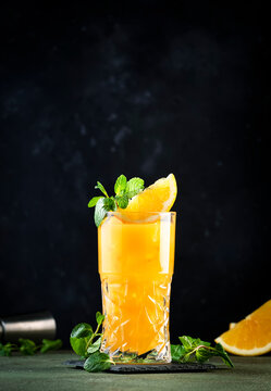 Screwdriver, classic alcoholic cocktail with vodka, orange juice and ice, garnished with fruit slice and mint. Dark background, bar tools