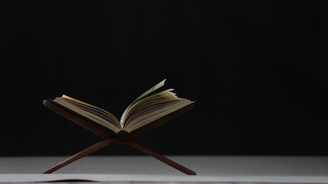 Slow motion of The Quran, the Muslim holy book, lies on a black background wooden board