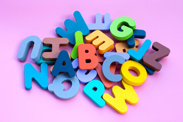 Colorful wooden alphabets on pink background.
