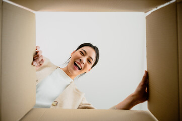 Surprised young asian woman unpacking. Opening carton box and looking inside. Packaging box,...