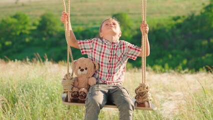 Happy boy is swinging on swing in park with his teddy bear toy. Son is swinging on swing in park,...