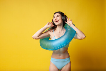 Obraz premium young curly slender brunette girl in a blue swimsuit in summer with an inflatable swim ring listens to music