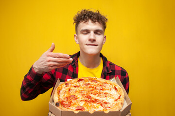 curly cute guy sniffs pizza and licks his lips on a yellow background, a man likes fast food