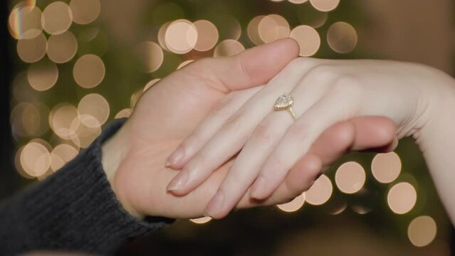 Mans hand putting wedding ring on womans hand in front of Christmas lights. 4K 24FPS