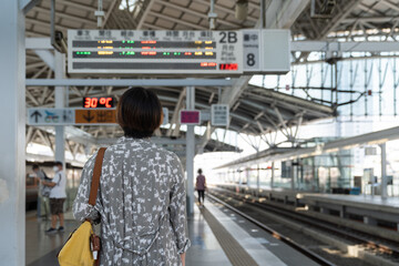 Theme travel public transport. rear back view of young Asian woman standing in front of time table and looks the schedule on a scoreboard in train station