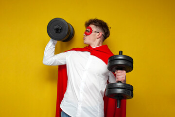 guy in a superman costume lifts heavy dumbbells and does sports on a yellow background, super hero...