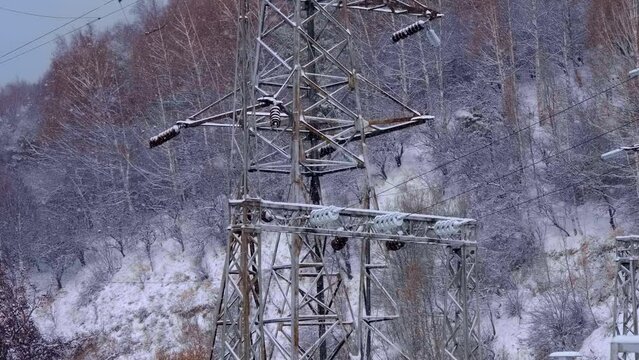 High-voltage wires with insulators on a metal mast near the transformer substation with wires, insulators, electric busbars, power transformer, switchgears, switching equipment in winter during a snow