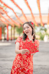 Woman wearing traditional cheongsam qipao costume holding ang pao, red envelopes in Chinese Buddhist temple. Chinese text means great luck