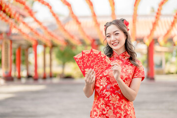 Portrait Beautiful Asian woman wearing traditional cheongsam qipao costume holding ang pao, red envelopes in Chinese Buddhist temple. Chinese text means great luck great profit. Emotion smile