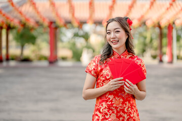 Young asian woman smiling happily holding ang pao, red envelopes wearing cheongsam looking confident in Chinese Buddhist temple. Celebrate Chinese lunar new year, festive season holiday