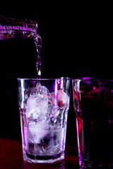Close-up bartender pours carbonated water into a glass with ice. Mixing alcohol cocktail in nightclub, pub, restaurant. Atmospheric pink lighting on a black background