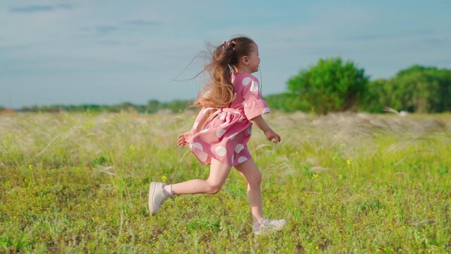 Happy running child in field. Happy family. Little happy girl runs on grass, smiles, in slow motion. Childhood dream concept. Cheerful little girl playing in park in summer. Kid runs across meadow.
