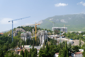 Construction cranes with new buildings under construction on the background of the mountain. Construction. Building architecture development. nature landscape background