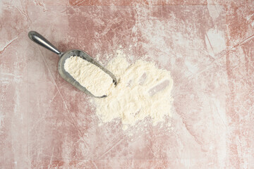 Stainless steel scoop with flour spilled out on a clear plastic mat on a pink marble countertop, preparation for baking
