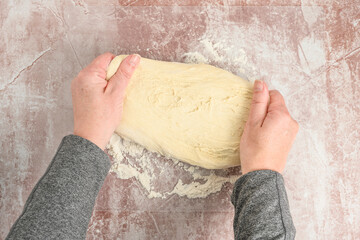 Woman’s hands pressing and spreading raw pizza dough on a clear plastic mat, preparation for baking 
