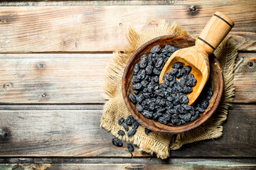 Raisins in a bowl with a wooden scoop.