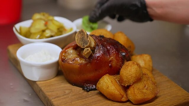 Meat dish in traditional Polish cuisine. Golonka z pieca - roasted pork knuckle with roasted potatoes, sauces, pickles and pepper shaker on wooden table. Top view. High quality 4k footage