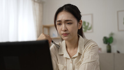 frustrated asian businesswoman troubled by a problem while working from home is propping head and...