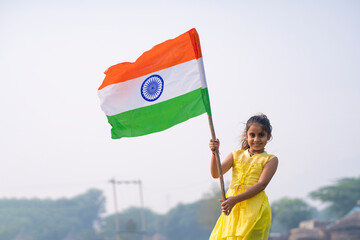 Cute indian little girl waving national tricolor flag at agriculture field.