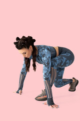 Beautiful athletic woman fitness instructor in blue camouflage tracksuit in starting position ready to sprint. Jogging. Starting pose isolated on a pastel pink background