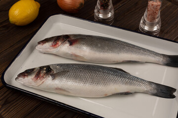 Two fresh sea bass fish on a metal baking sheet